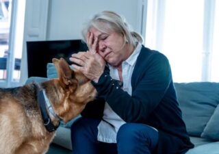 Older woman sitting with one hand on head and the other petting her dog